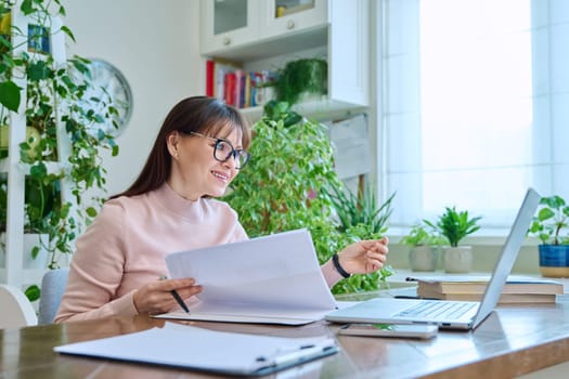 Woman working remotely in home office at workplace with computer. Female professional holding paper contract in hands, architect lawyer accountant preparing documents. Work remotely business freelance