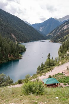 Lake surrounded by snowy mountains, crystal clear water, blue sky, hazy clouds, fresh air. Small house on shore of lake.