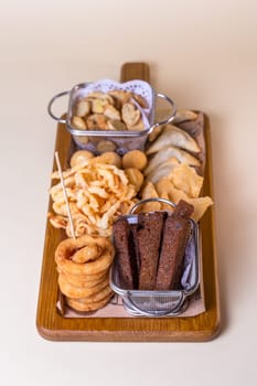 Top view beer platter with croutons, onion rings, chips on a wooden board.