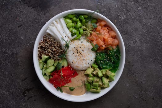 Top view of a bye bowl with salmon, avocado, cucumber, sprouts and rice on a white plate.