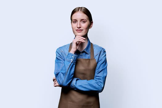 Portrait of young smiling confident woman in apron on white studio background. Successful positive female looking at camera. Worker, startup, small business, service sector, staff, youth concept