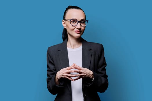 Portrait of thinking serious 30s business woman on blue studio background. Confident female in glasses, suit looking at camera. Business work teaching job career people concept