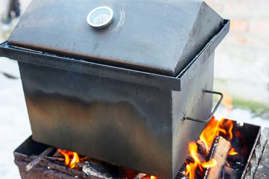 Smoker box over open flame outdoors with temperature gauge. Outdoor cooking and barbecue concept.