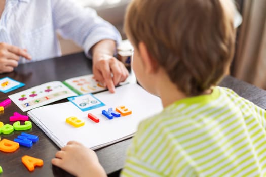 Boy at wooden table with colorful magnetic letters. Early education and learning concept.