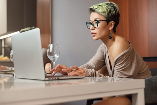 a beautiful girl with short hair and glasses is sitting indoors at a laptop chatting and working online