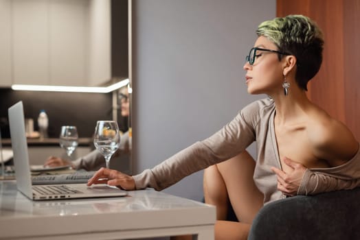 A sexy girl with short hair and glasses is sitting indoors at a laptop, chatting and working online