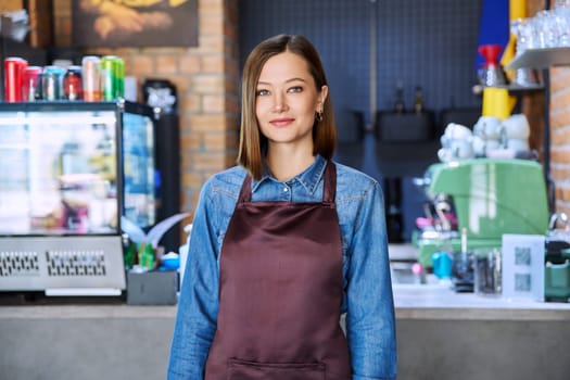 Confident successful young woman service worker in apron looking at camera in restaurant cafeteria coffee shop pastry shop. Small business, staff, occupation, entrepreneur owner, work concept