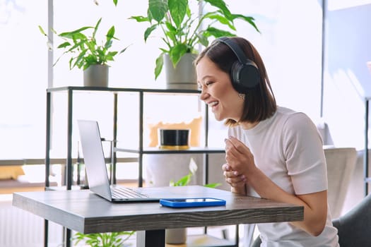 Young woman in headphones having video chat conference call using laptop computer sitting in coworking cafe. Female college student studying online listening webinar preparing exam, working remotely