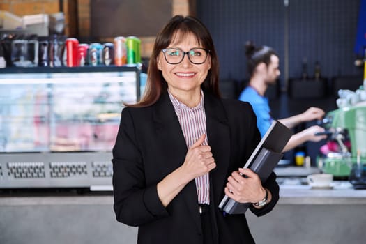 Portrait of confident business woman accountant financier lawyer small business owner. Successful middle-aged female with laptop in hands looking at camera, background coffee shop cafeteria restaurant