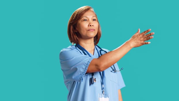 Close up shot of clinic worker doing swiping hand motion gestures, remotely controlling digital screen. Experienced nurse isolated over blue studio background working in high-tech modern hospital
