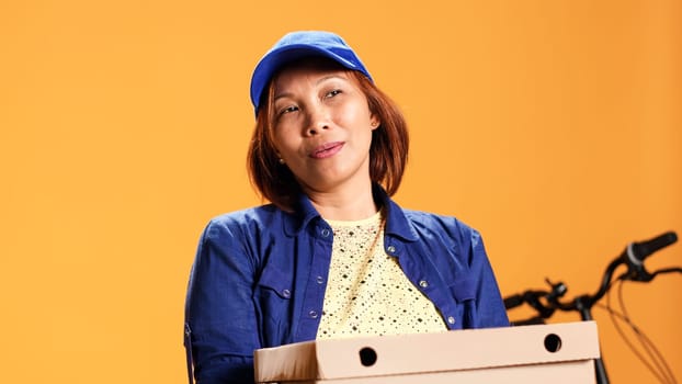 Hasty BIPOC employee waiting for client to answer door and pick up meal order. Portrait of bored courier isolated over studio background carrying stack of pizza boxes, close up