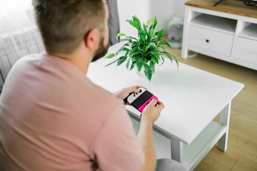 Cheerful young man seated on a sofa playing video games at home. Gaming addiction and entertainment.