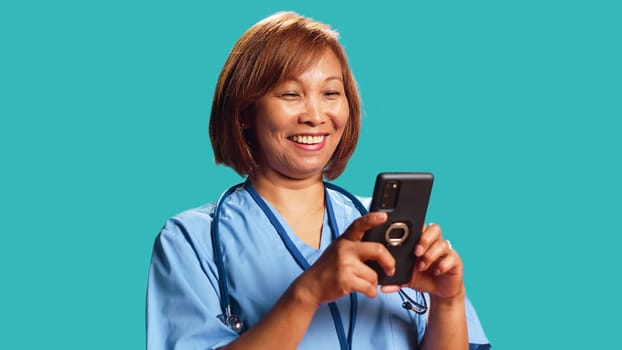 Jubilant nurse having burst of joy at work while chatting with friends, isolated over studio background. Elated hospital worker delighted about great news she received over the phone, close up