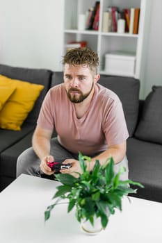 Young man spending time at home, sitting on a couch in apartment and playing arcade car video games on console. Male using controller to play street racing drift simulator