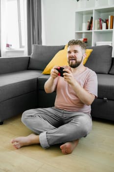 Cheerful young man seated on a sofa playing video games at home. Gaming addiction and entertainment.