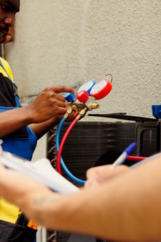 Professional workers assigned to do air conditioner check, refilling freon. Expert repairmen team using ac gauges vacuum pump to skilfully measure the pressure in HVAC system