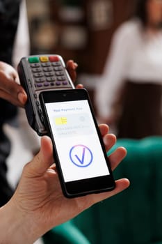 Detailed view of concierge helping elderly retired man with payment using cellphone and NFC technology. Close-up shot of male traveler paying using mobile device with assistance of hotel employee.