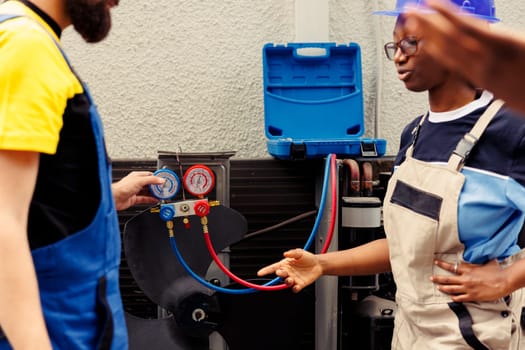 Licensed technicians team working with manifold gauges to check air conditioner refrigerant in need of maintenance. Qualified mechanics using barometer benchmarking hvac system component