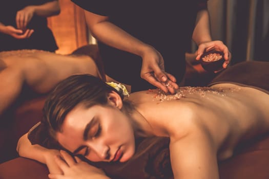 Couple customer having exfoliation treatment in luxury spa salon with warmth candle light ambient. Salt scrub beauty treatment in Health spa body scrub. Quiescent