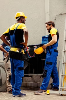 Diverse team of knowleadgeable engineers brainstorming possible ways to recondition damaged outdoor hvac system. Certified repairmen coworkers commissioned to repair broken air conditioner