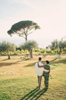 Man and woman walk hugging along a green lawn. Back view. High quality photo