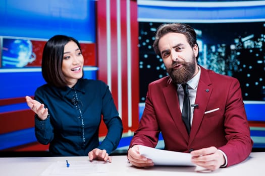 Diverse journalists reading daily headlines in studio, using media outlets papers to address latest information and updates about incidents. Presenters team reporting live for tv network.