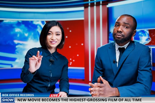 Reporters present new movie breaking charts, news report analysts talking about film bringing down box office records. Team of diverse journalists reading headlines, daily events.