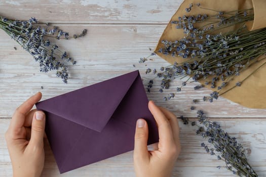 Flat lay composition of female hands holding violet envelope with dry lavender flowers. Copy space template mock up. Top view. Concept of Wedding invitation postcard. Business advertisement brand blank