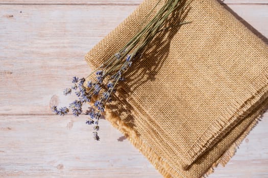 Dried lavender flowers on burlap textile material on wooden background. Copy space for your text. Advertisement mock up template
