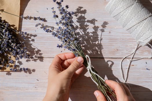 Top view flat lay of process making bouquets of dried lavender flowers. Cotton rope, scissors. Female do homemade herbs bouquet. Preparing for winter