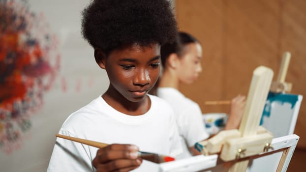 African boy painting canvas with watercolor while happy caucasian girl draw cool tone picture at colorful stained wall. Multicultural highschool student attend creative activity together. Edification.
