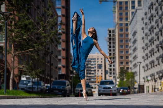 Beautiful Asian ballerina in blue dress posing in splits outdoors. Urban landscape