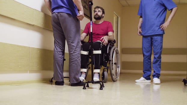 Tired disabled young man sitting in a wheelchair. Doctor helping him.