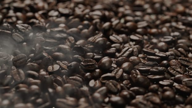 Close up of fresh brown coffee bean with roasted smoke from pile of coffee beans. Macrography of hot coffee seed with fragrant and scented hot smoke come from pile of bean. Top down view. Comestible.