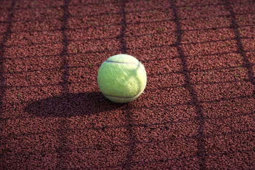 Yellow tennis ball is resting on a tennis hardcourt surface, empty court with no players, equipment or any notable activity present