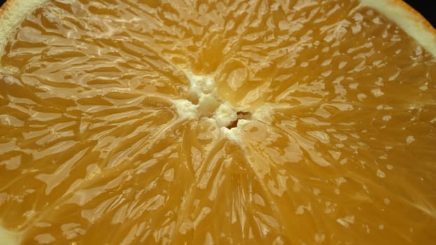 A macrography capture of an orange slice, placed against a sleek, isolated black backdrop, unfolds as a visual masterpiece of citrus allure. A slice of orange with black background. Comestible.