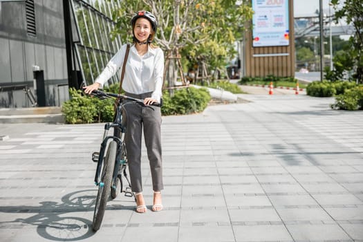 In a city setting Asian businesswoman in a suit and helmet smiles beside her bicycle ready for her morning commute. portrays the cheerful blend of work and outdoor activity in business commuter life.