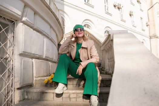 A woman in a green outfit is sitting on a set of stairs. She is wearing a green hat and sunglasses