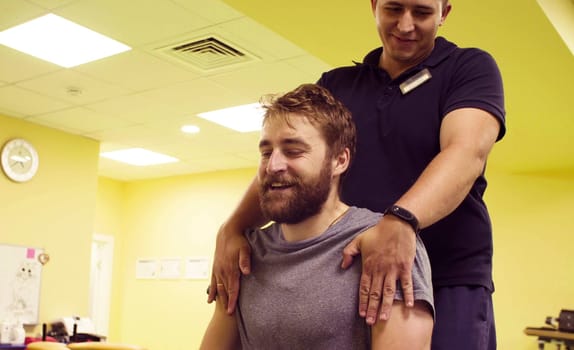 Young disabled man doing exercises at the rehabilitation center. Doctor physiotherapist helping him. Healthy gymnastics. Active people.