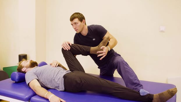 Doctor physiotherapist doing stretching exercises for young disable man at the rehabilitation clinic