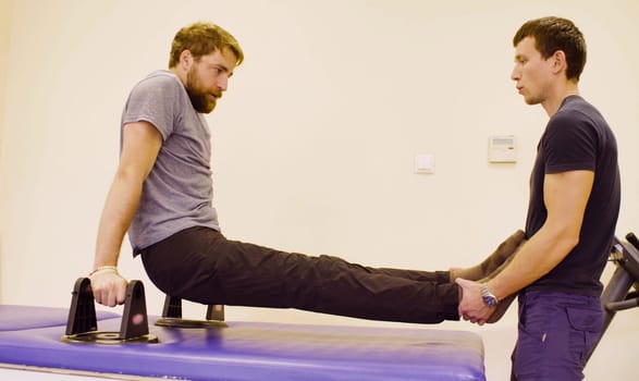 Doctor physiotherapist helping young disable man to do the recovery exercise at the rehabilitation clinic