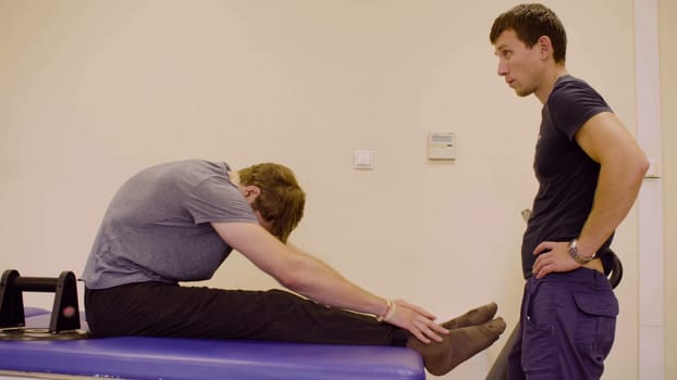 Doctor physiotherapist helping young disable man to do the recovery exercise at the rehabilitation clinic