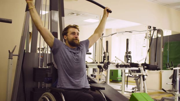 Young disabled man in wheelchair doing strength exercises for hands at the rehabilitation clinic