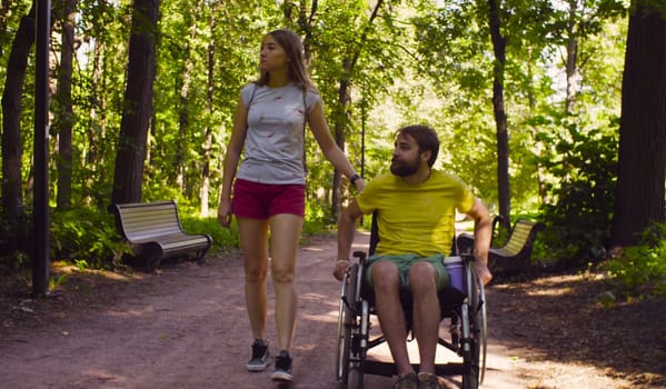 Young disable man in a wheelchair on a walk in the park with his wife.