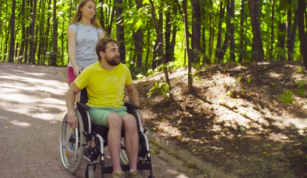 Young disable man in a wheelchair on a walk in the park with his wife.