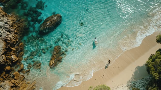 An aerial view of two individuals standing on the beach, overlooking the azure waters with surfboards in hand AIG50