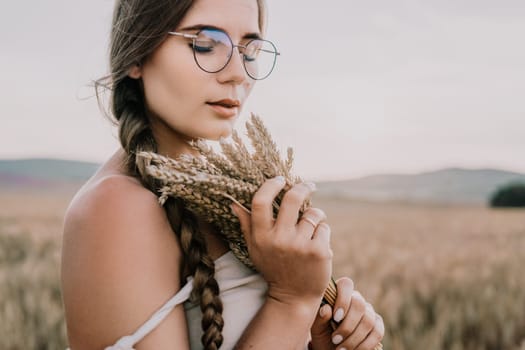 A woman is holding a bunch of wheat in her arms. The wheat is dry and brown, and the woman is wearing a white dress. The scene is set in a field, and the woman is posing for a photo