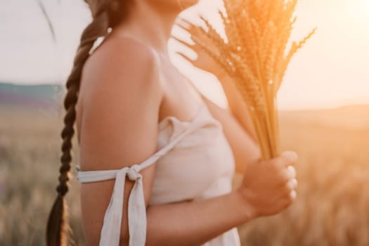A woman is holding a bunch of wheat in her arms. The wheat is dry and brown, and the woman is wearing a white dress. The scene is set in a field, and the woman is posing for a photo
