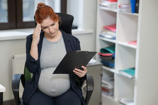 Pregnant woman reading documents on a paper tablet in the office