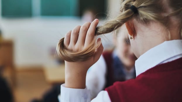 A girl touches a ponytail of her hair during class